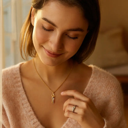Woman wearing a pink sweater and gold necklace with a small pendant, indoors.