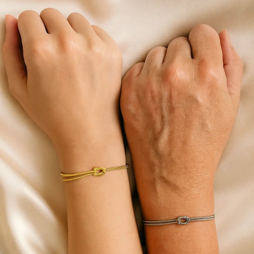 Two wrists with gold and silver bracelets on a beige fabric background