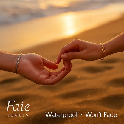 Two hands holding fingers on a beach with sunset, featuring Faie Jewels branding.